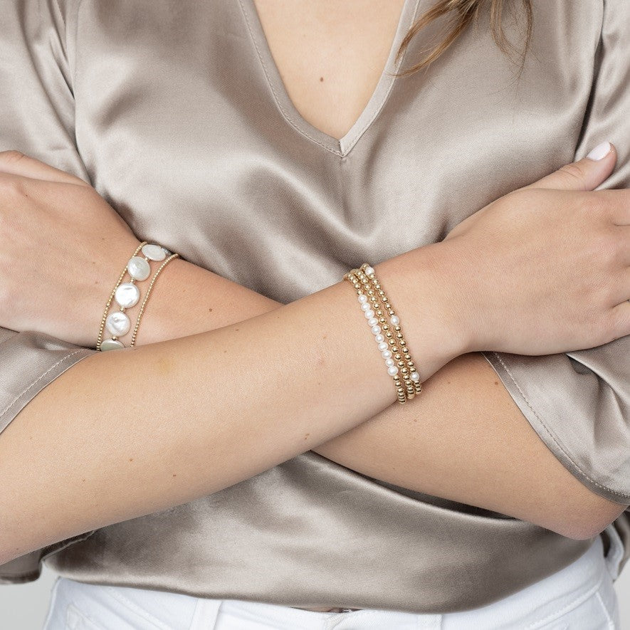 Model wearing coin pearl and gold beaded bracelets