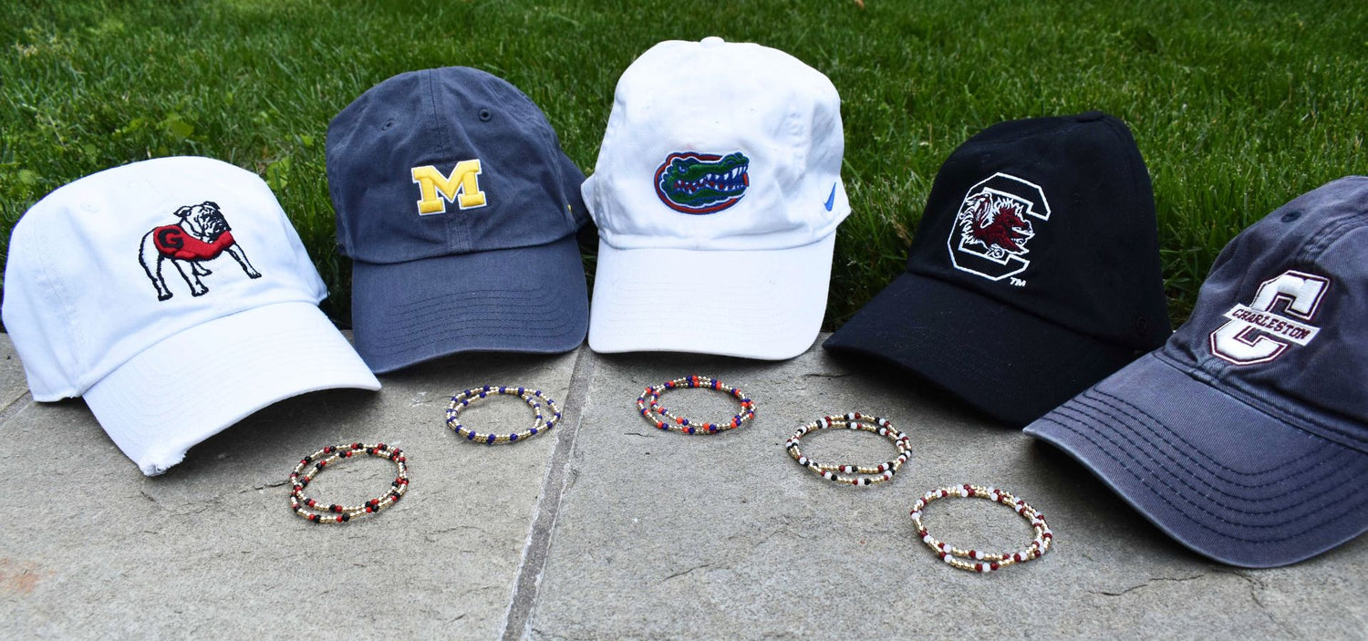 Collection of baseball caps with different logos and bracelets  on a concrete surface with grass in the background