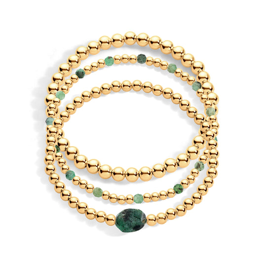 A three-layered stack of gold-filled stretch bracelets featuring emerald accents.