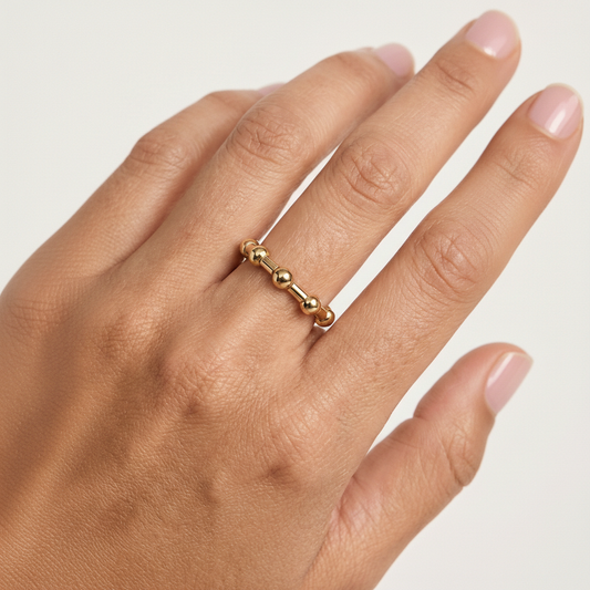 Gold beaded ring on a hand against a neutral background