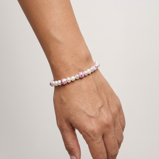 Pearl bracelet with pink accents on a wrist against a plain background