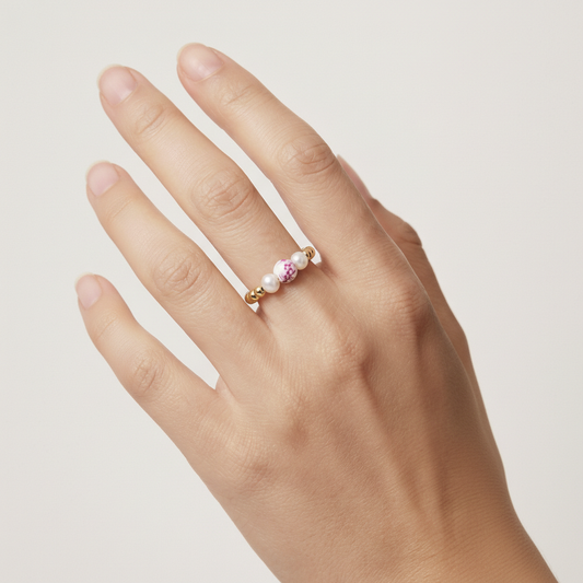 Hand wearing a gold ring with pink gemstones on a light background