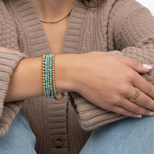 Model wearing multiple gold-filled and turquoise gemstone bracelets