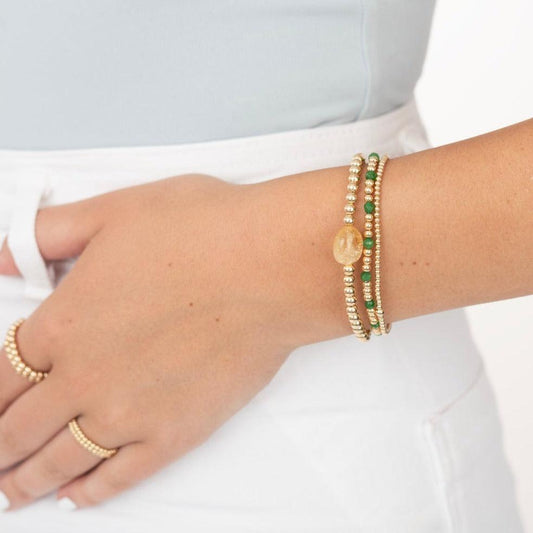 Womans wrist showing 3 gold filled bracelets with emerald gemstones