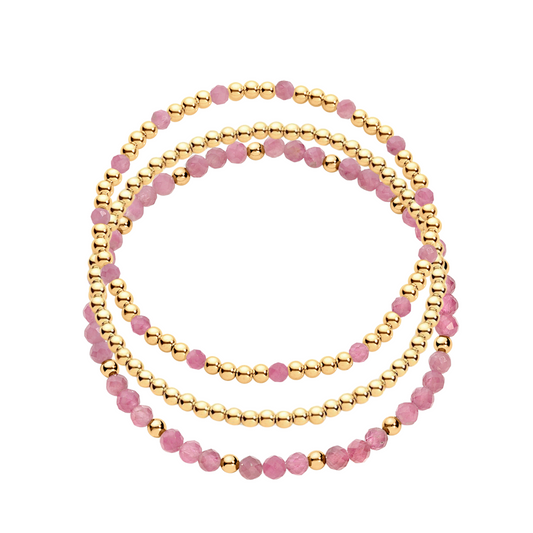 A stack of three bracelets, one featuring gold-filled beads and another with gold-filled beads and pink gemstones.