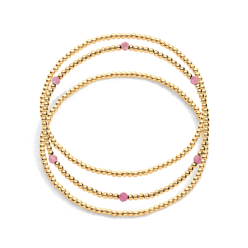 A stack of three gold-filled bracelets with pink  gemstones on a white background.