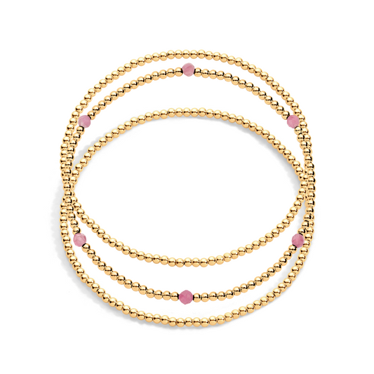 A stack of three gold-filled bracelets with pink  gemstones on a white background.