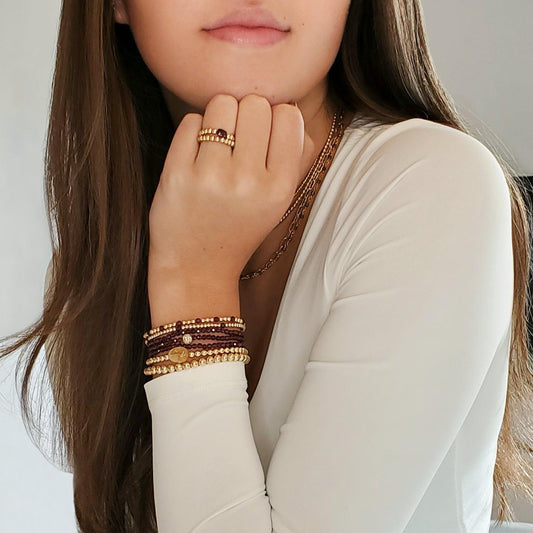 Model wearing gold filled beaded bracelet and rings with garnet colored gemstones